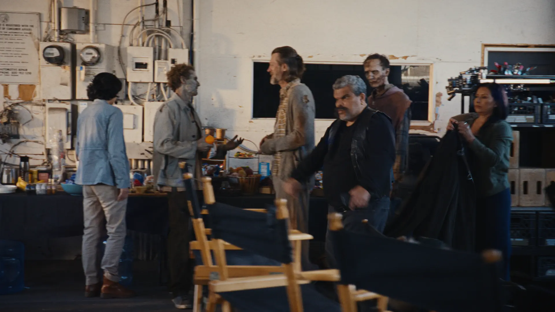 Luis Guzman walks by a craft services table, where a line of zombies is eating food and conversing