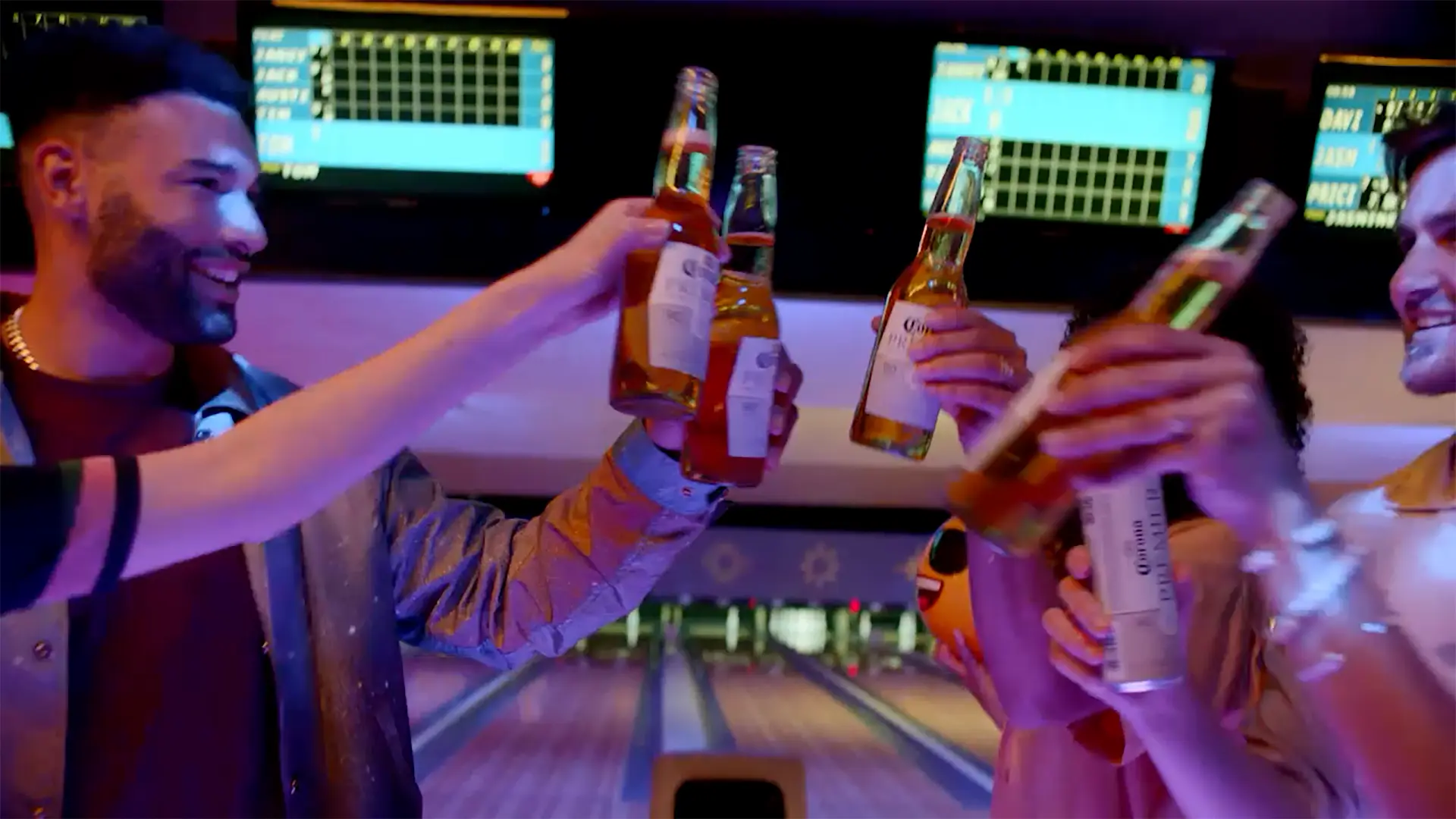 friends at a bowling alley toast with bottles of Corona Premier