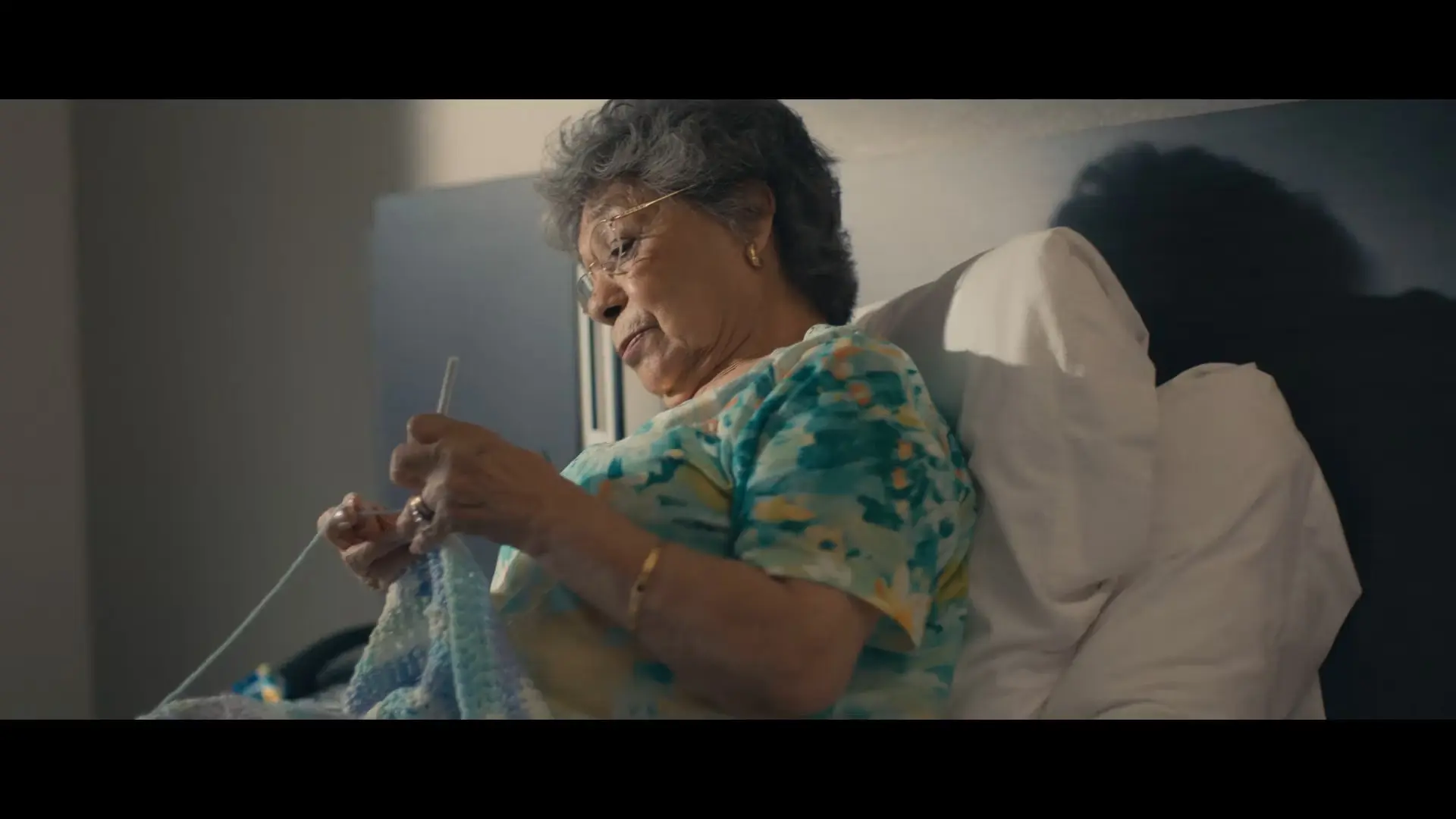 a grandmother in a hotel bed knitting a baby blanket