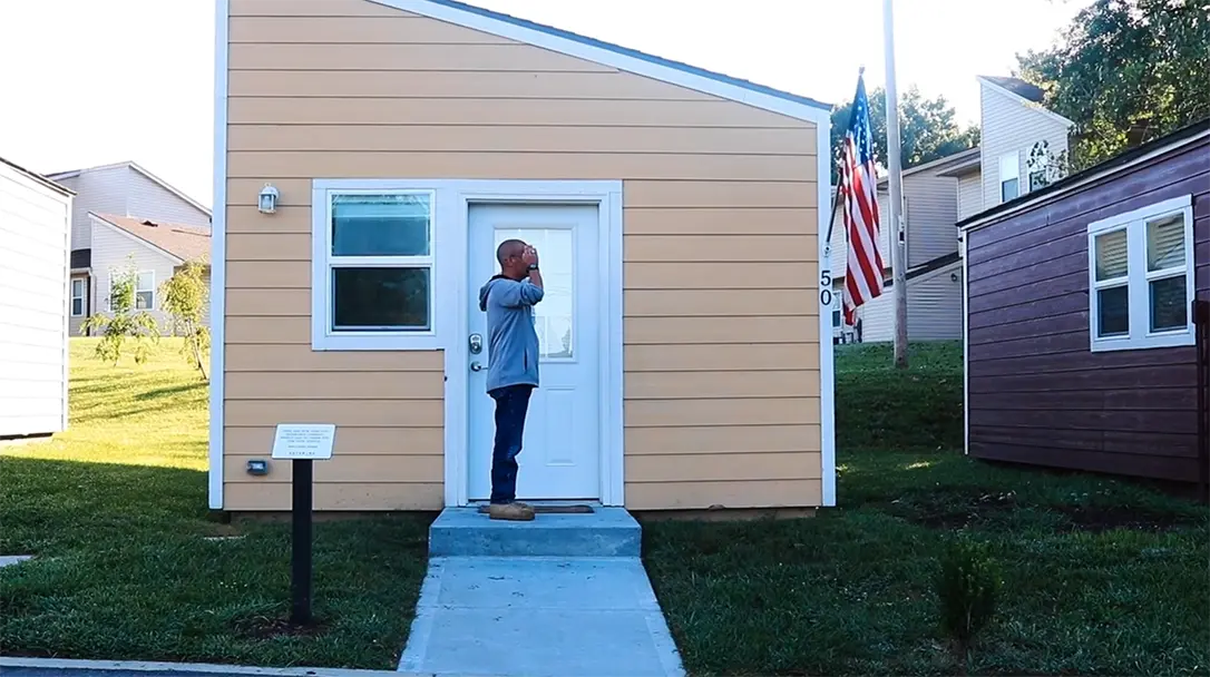 a veteran standing in front of a small shotgun shack